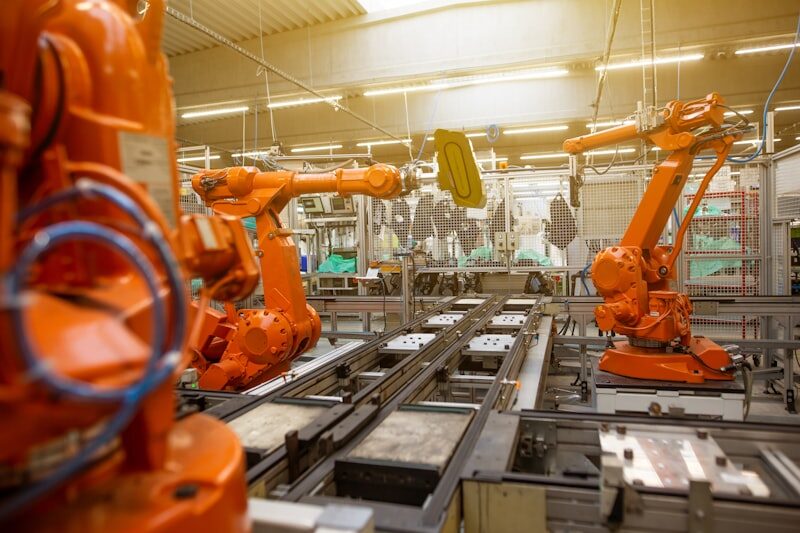 Orange industrial robotic arms on automated assembly line for Uni-Weld™ UV plastic bonder electronics assembly